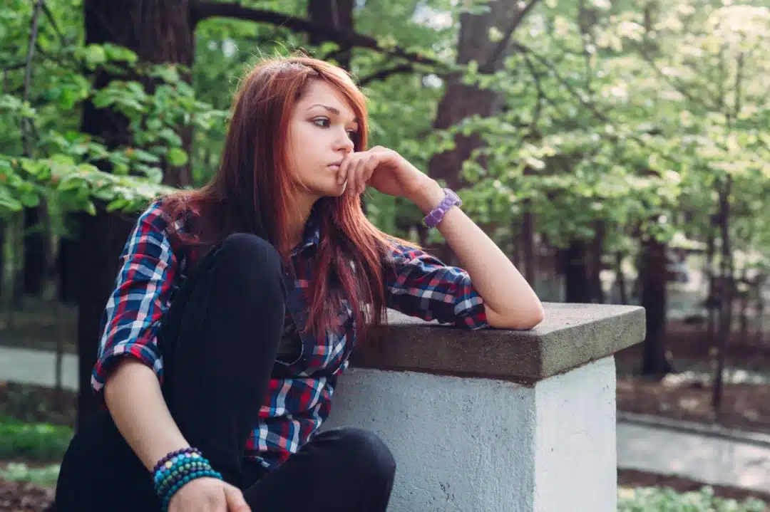 zamyślona dziewczyna nastolatka, siedzi na murku